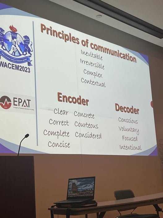 A person sitting at a podium in front of a large screenDescription automatically generated